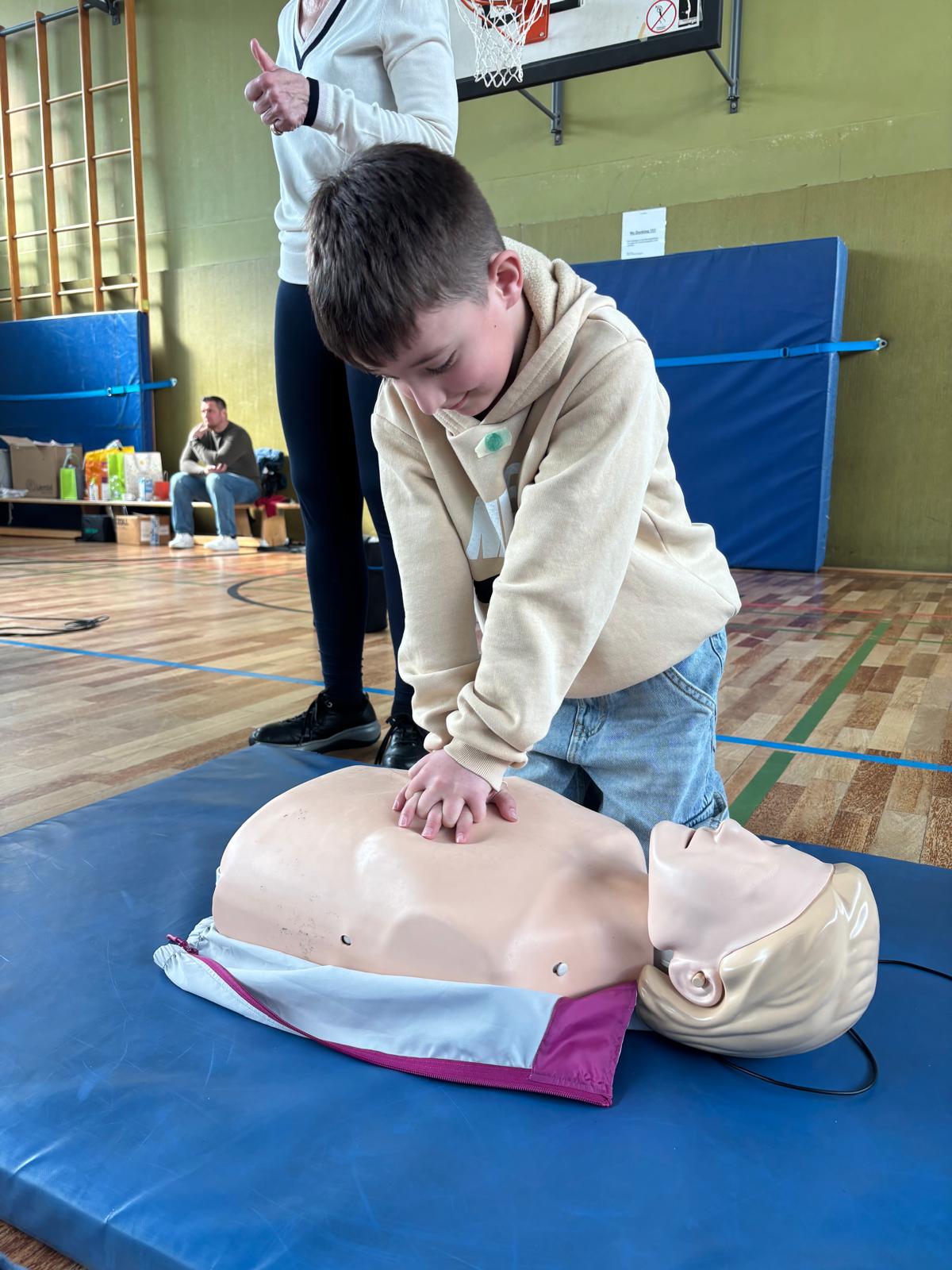 Kind übt Herzdruckmassage an einer Trainingspuppe